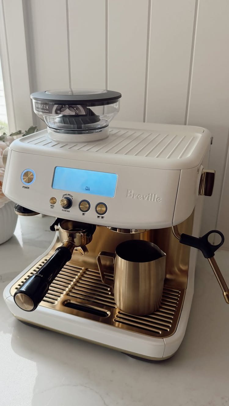 White Breville espresso machine with gold accents and a gold milk pitcher.