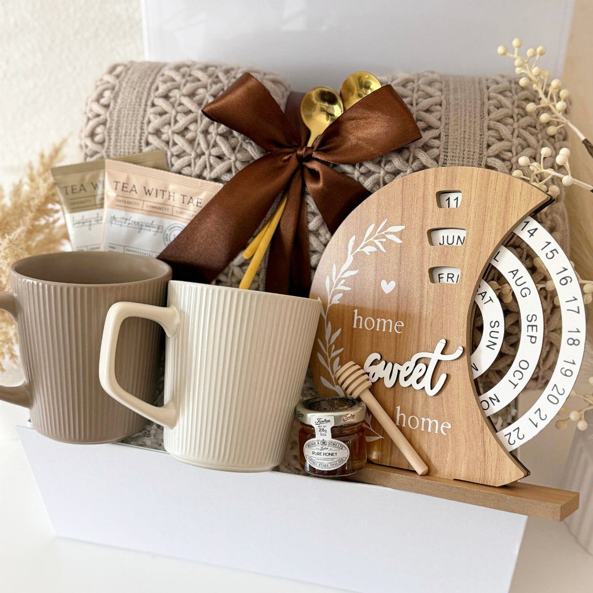 Gift box with ceramic mugs, tea bags, honey, and a wooden home calendar.
