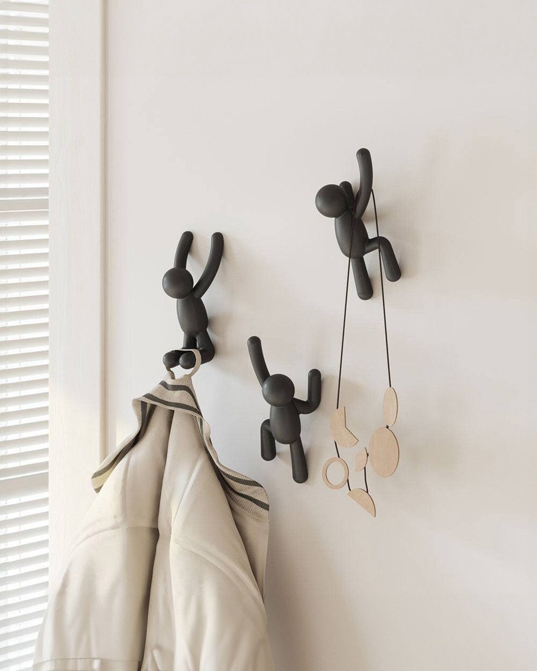 Black human-figure wall hooks holding a beige jacket and decorative ornaments on white wall