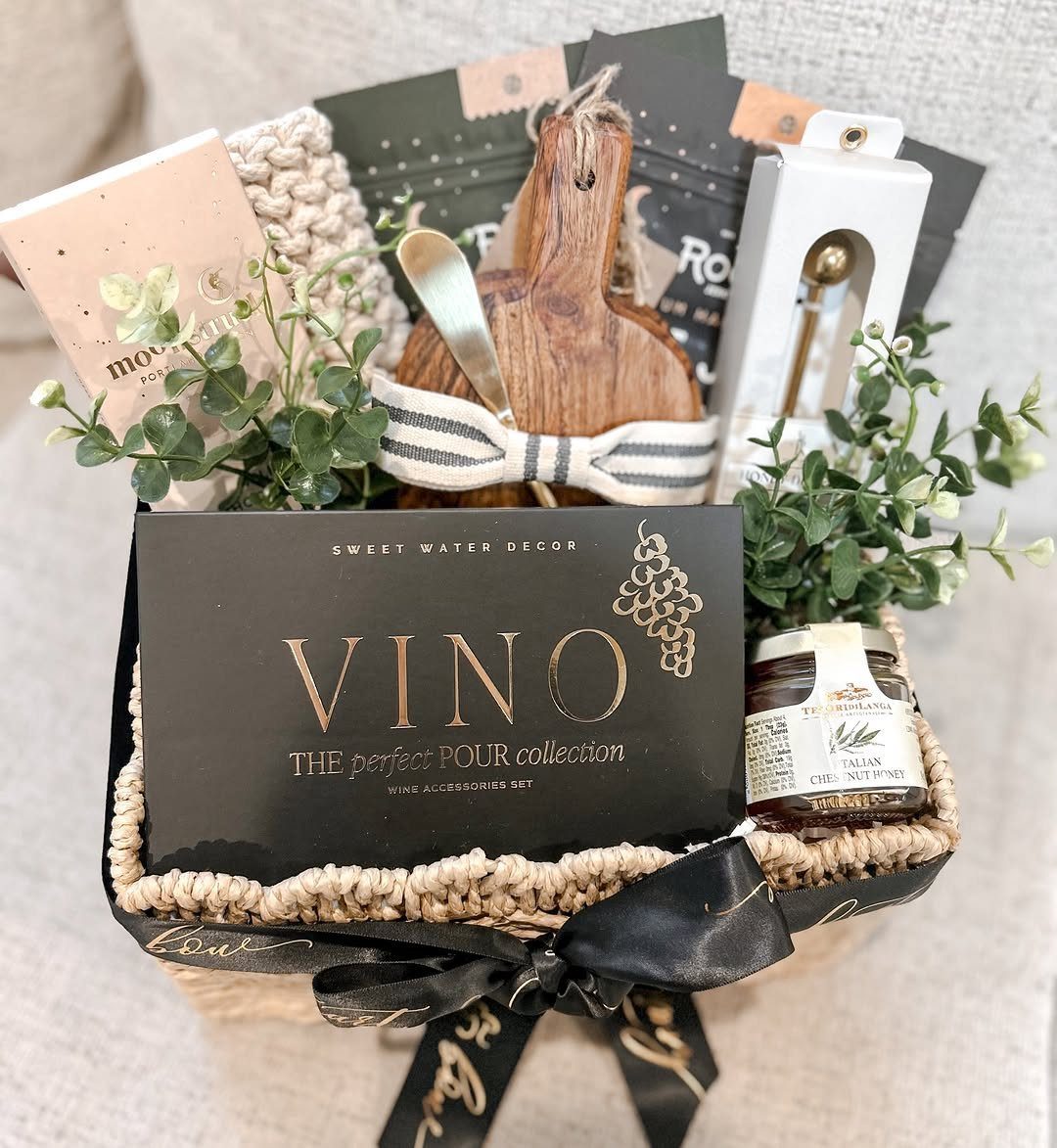 Woven gift basket with wine accessories, a wooden board, and a jar of preserves.