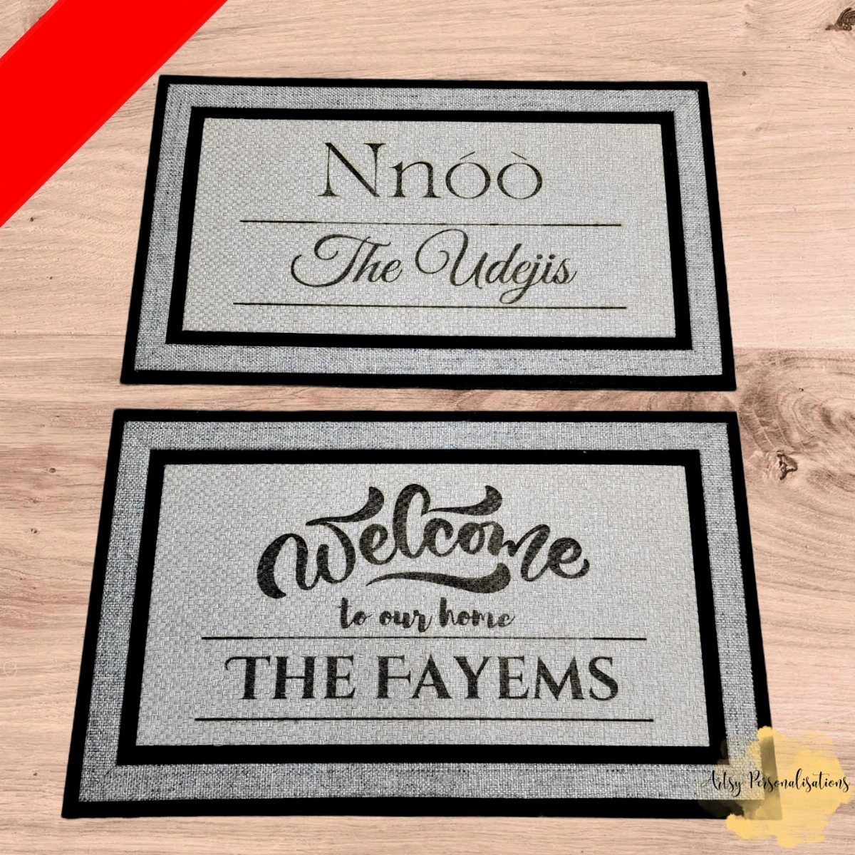 Two personalized grey doormats with black borders and custom family names on wood.