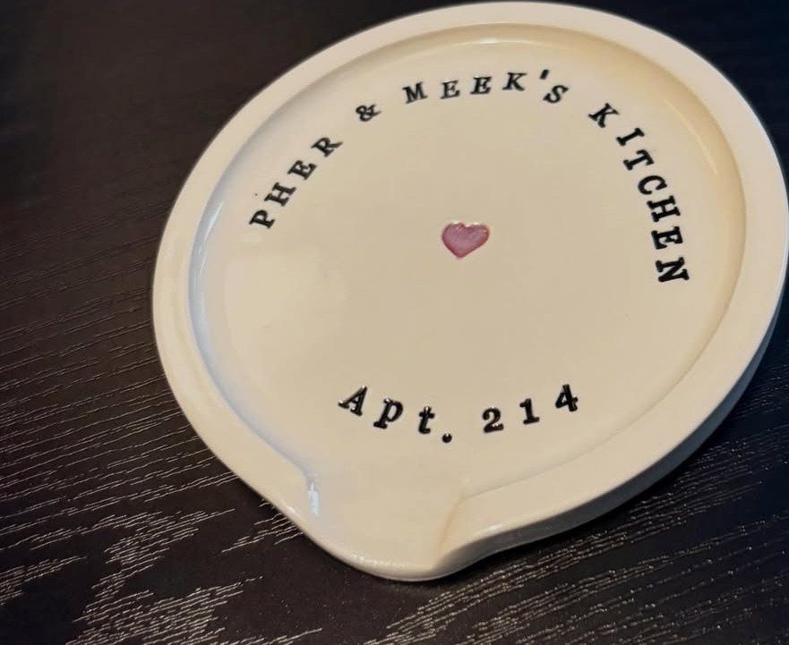 White ceramic spoon rest with personalized kitchen text and a small pink heart.