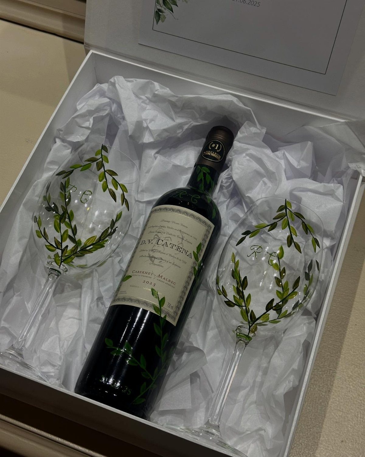 Bottle of red wine and two leaf-patterned glasses in a white gift box