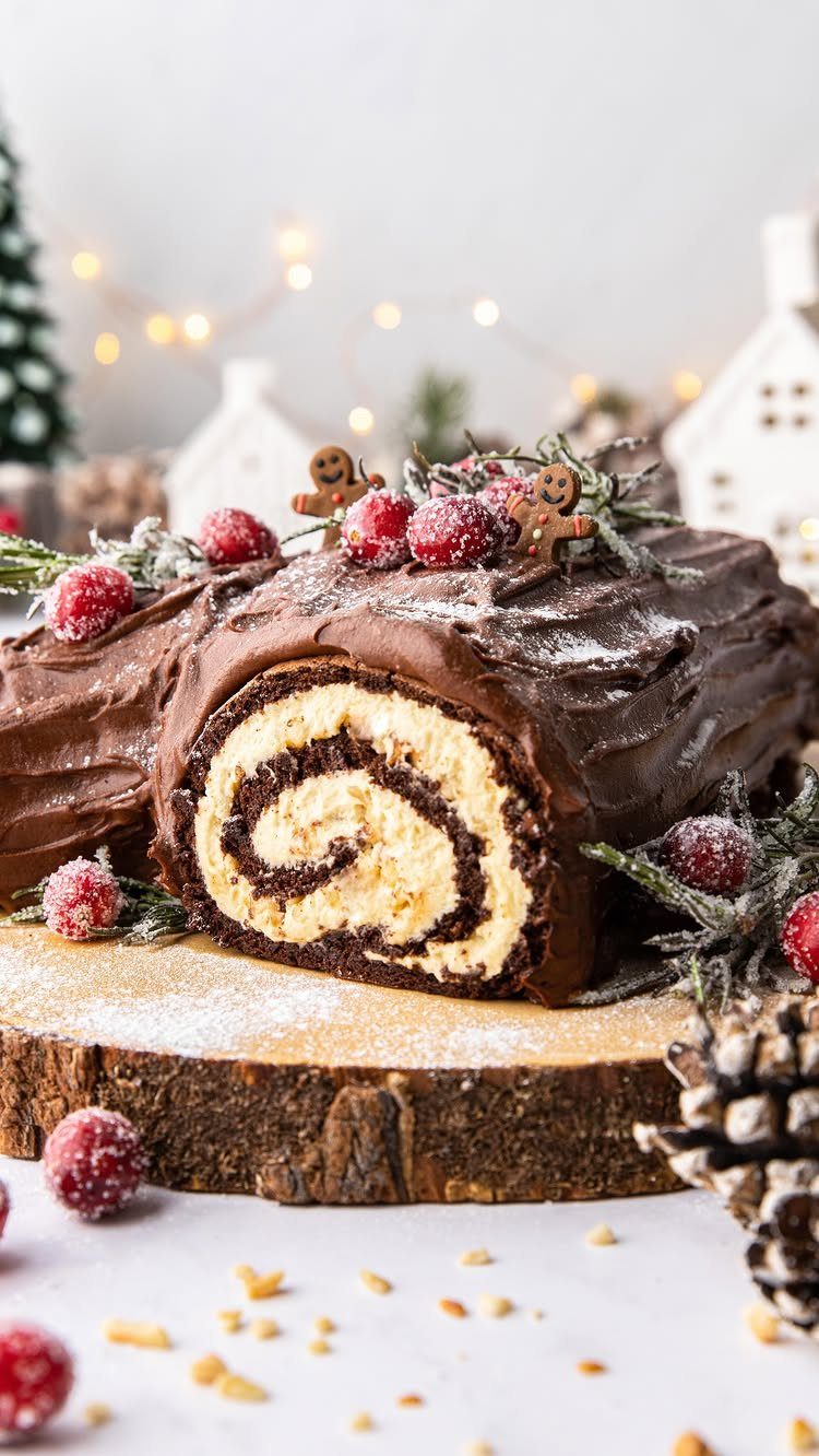 Chocolate Bûche de Noël cake decorated with berries and gingerbread on a wooden platter.