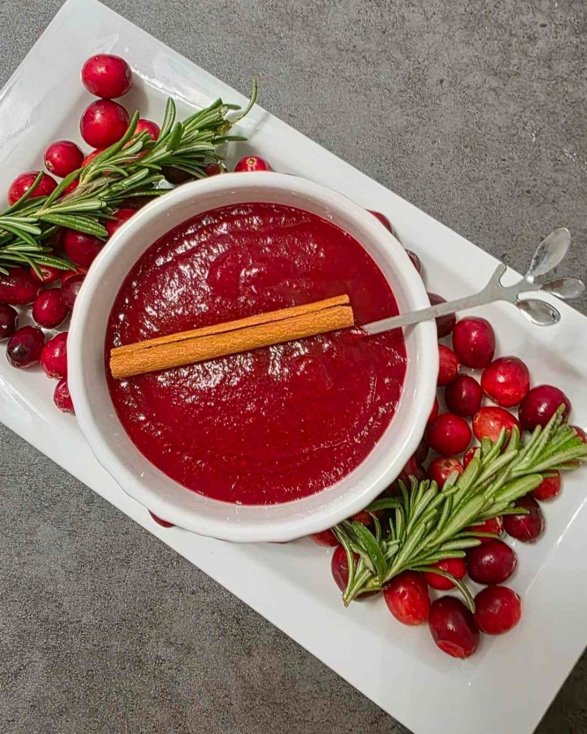 Cranberry sauce in a white bowl garnished with cinnamon, cranberries, and rosemary sprigs.