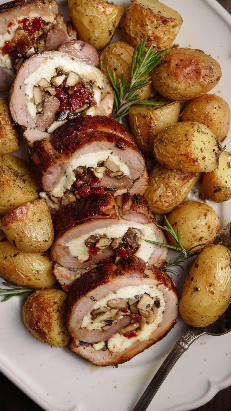 Stuffed pork tenderloin slices with roasted potatoes and rosemary on a white platter.