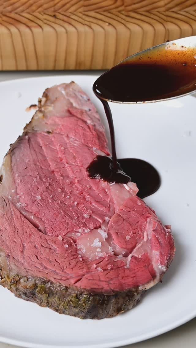 Prime rib beef slice on a white plate with dark sauce being poured.