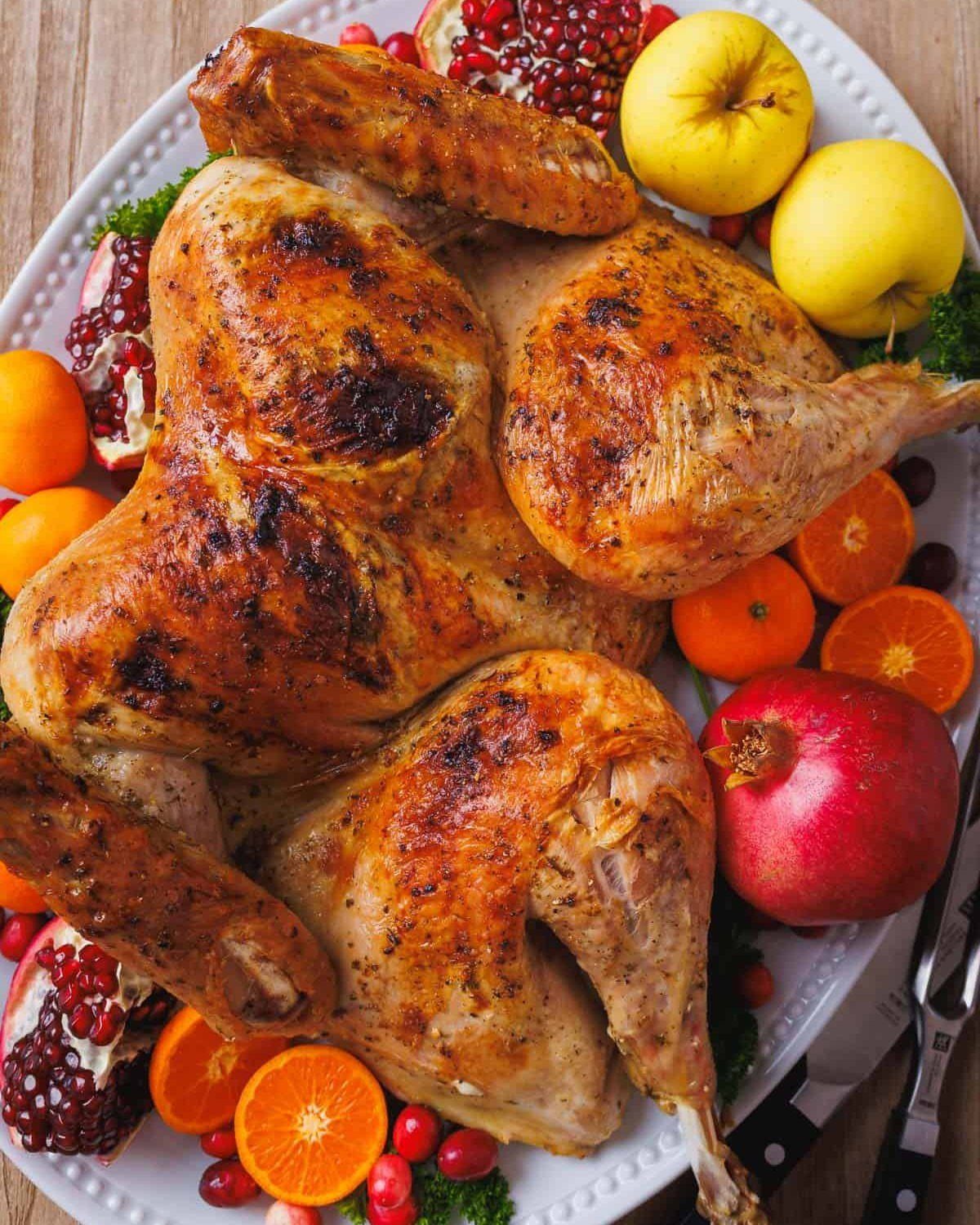Roasted turkey on a white platter garnished with apples, pomegranates, and orange slices.