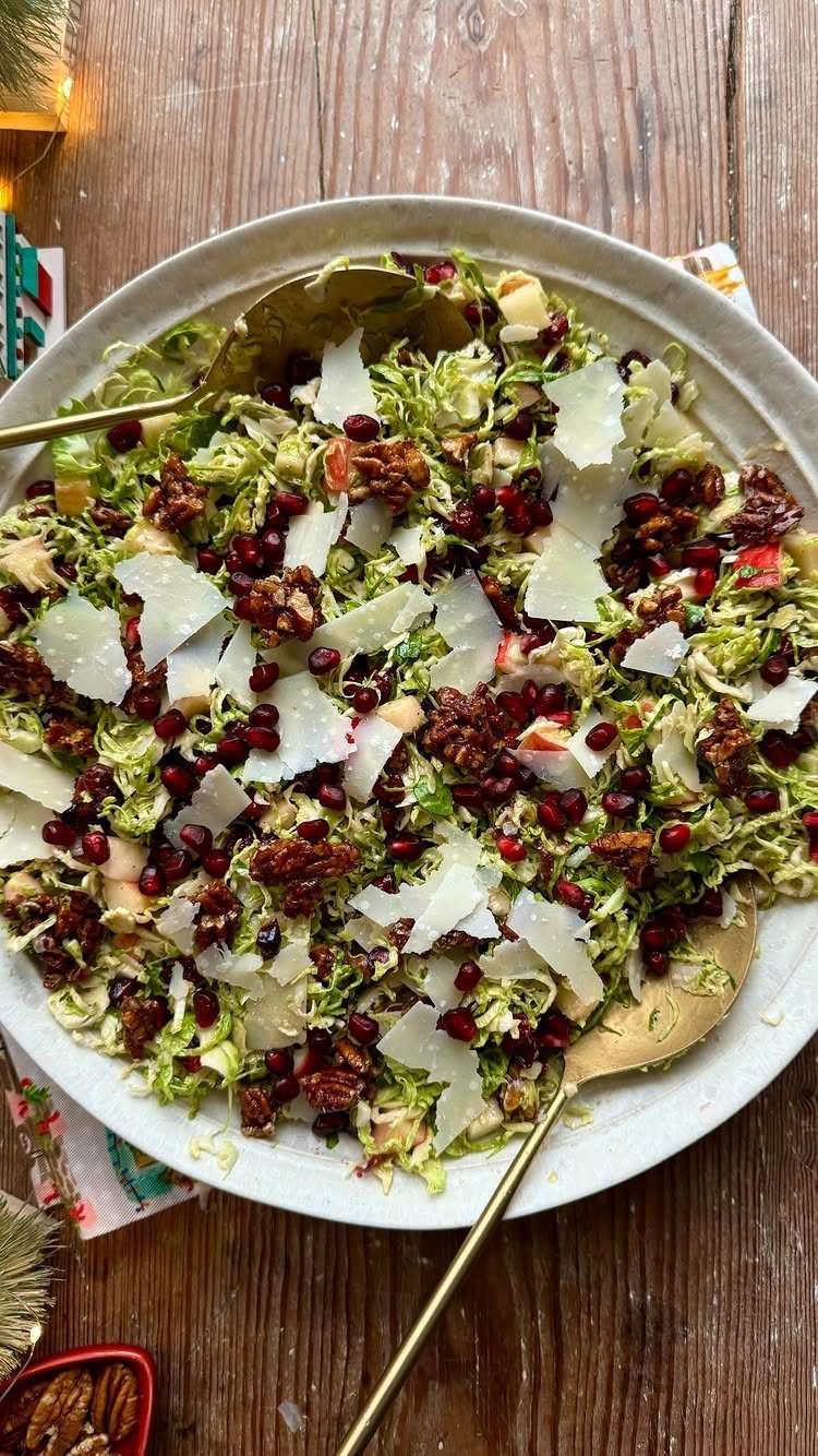 Shredded green salad with pomegranate seeds, pecans, and shaved cheese in a bowl.