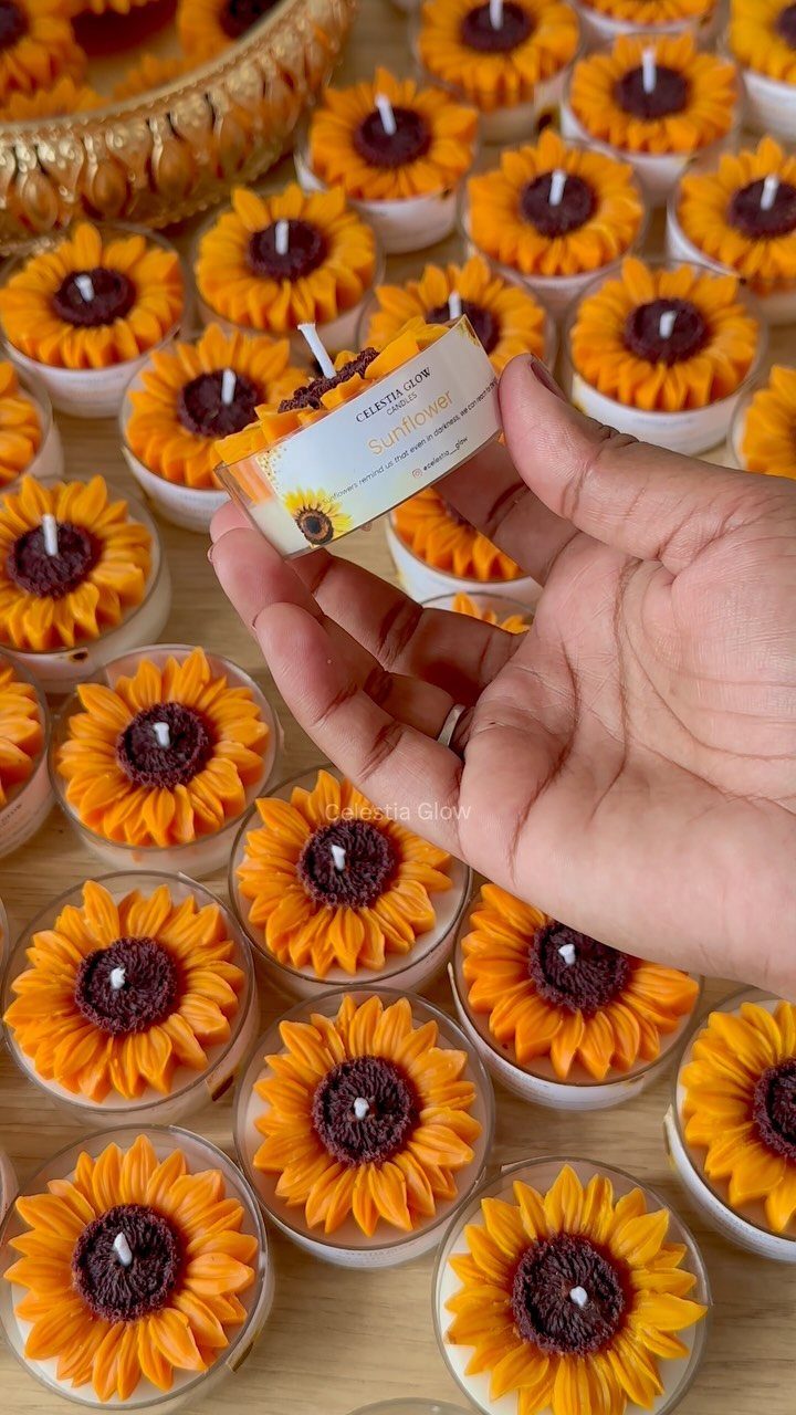 Sunflower shaped candles in glass jars arranged on a light wooden table.