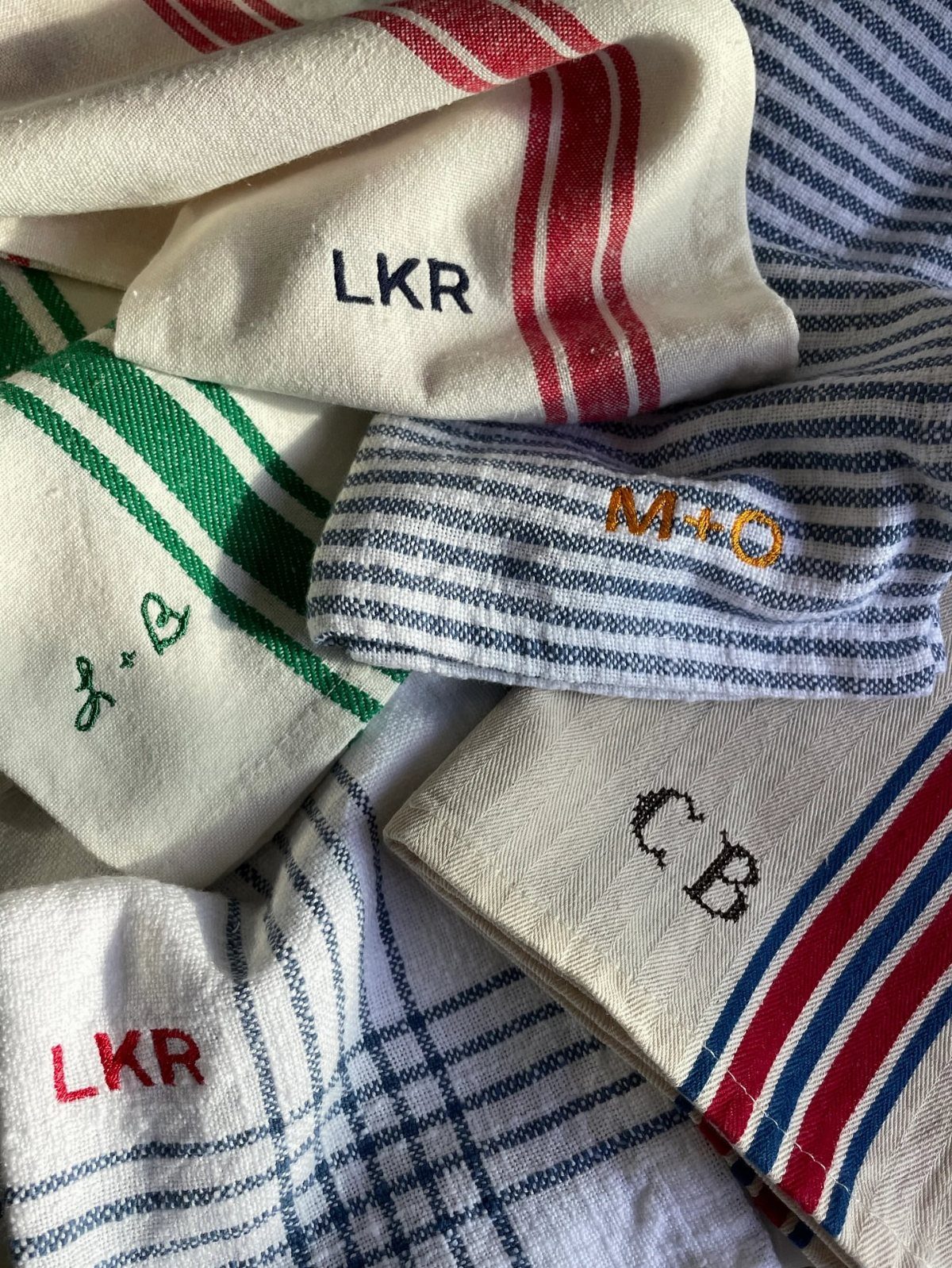 Folded white kitchen towels with colorful stripes and embroidered personalized initials.