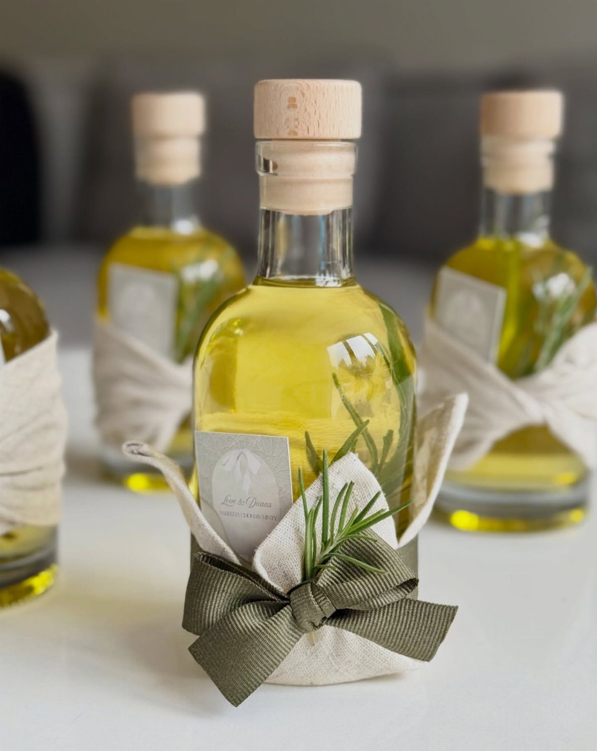 Olive oil bottles wrapped in white fabric and green ribbons with rosemary sprigs.