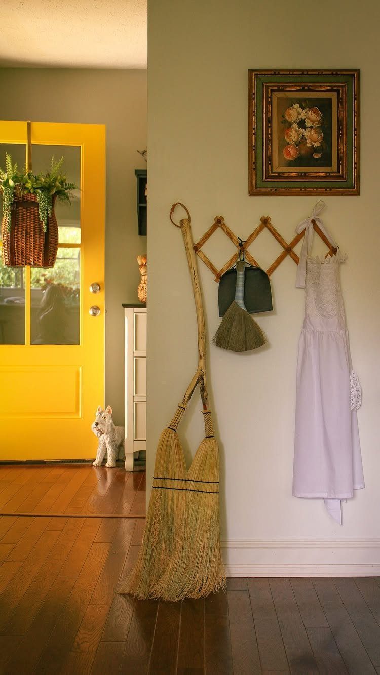 Straw broom, dustpan, and white apron hanging on a wooden wall rack indoors.