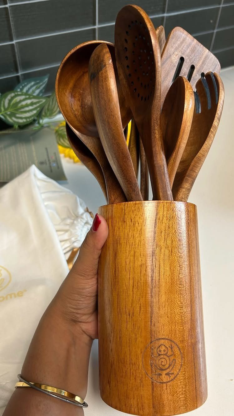 Wooden kitchen utensils in a matching wooden holder held by a hand.