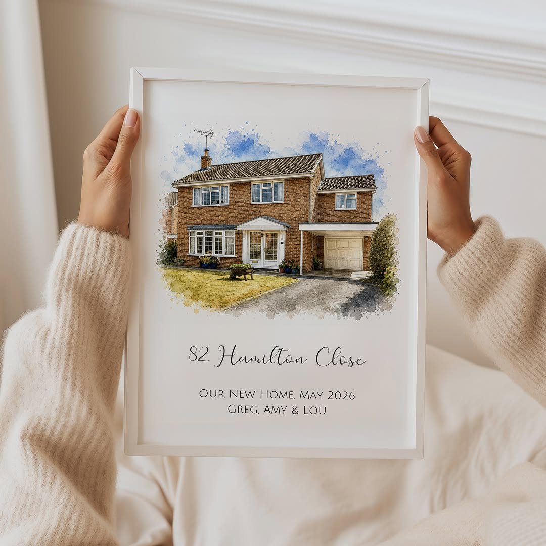 Framed watercolor house portrait with personalized address held by a person in beige.