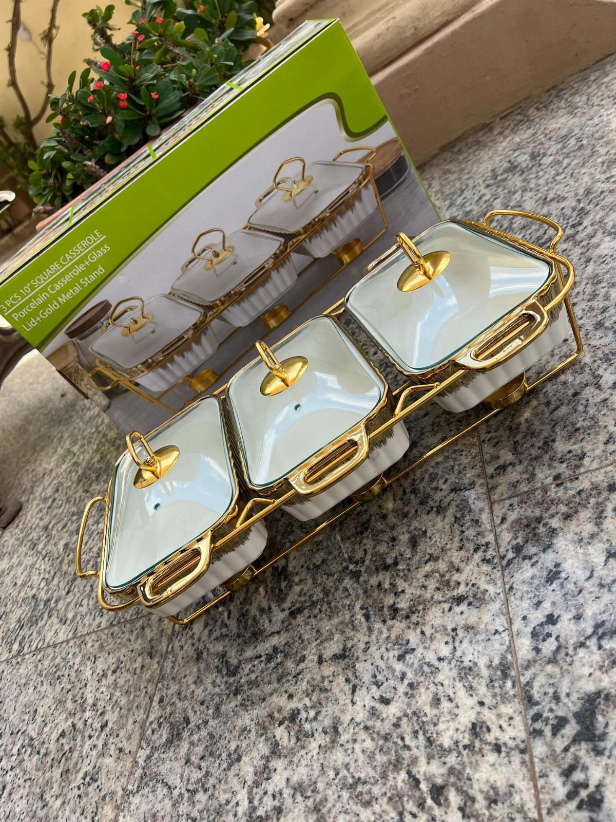 White porcelain casseroles with gold lids in a gold metal stand next to box