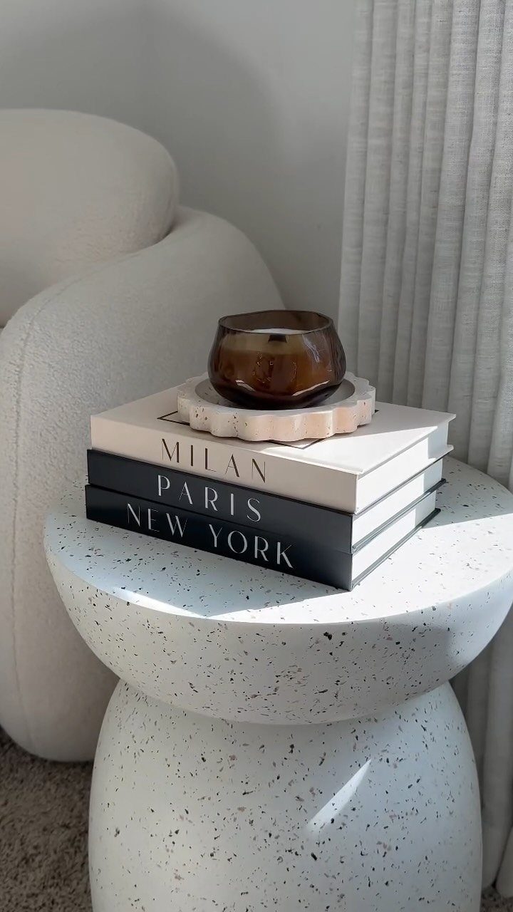 Stacked coffee table books with city names topped with a brown candle holder.