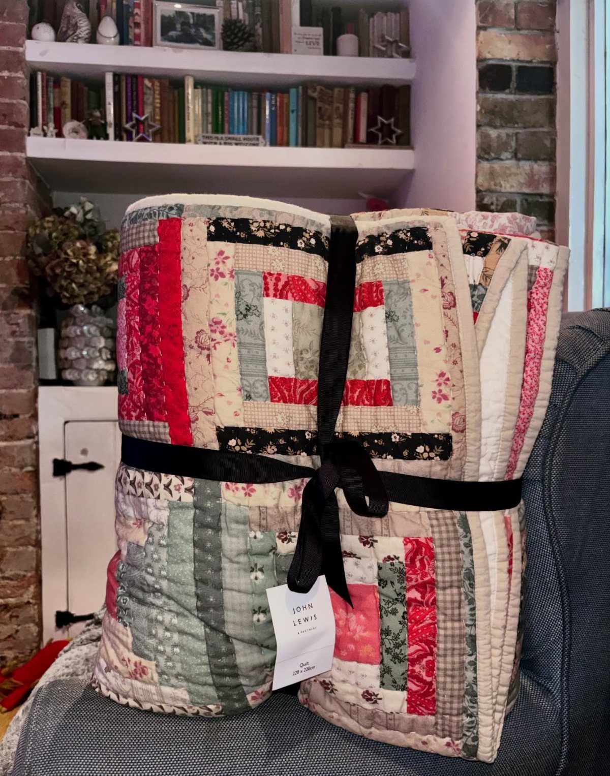 Patchwork quilt tied with a black ribbon and gift tag on a sofa