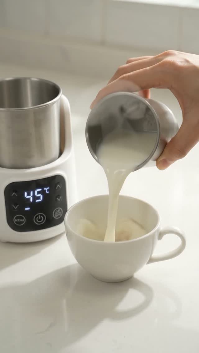 Frothed milk being poured into a white cup next to an electric frother.