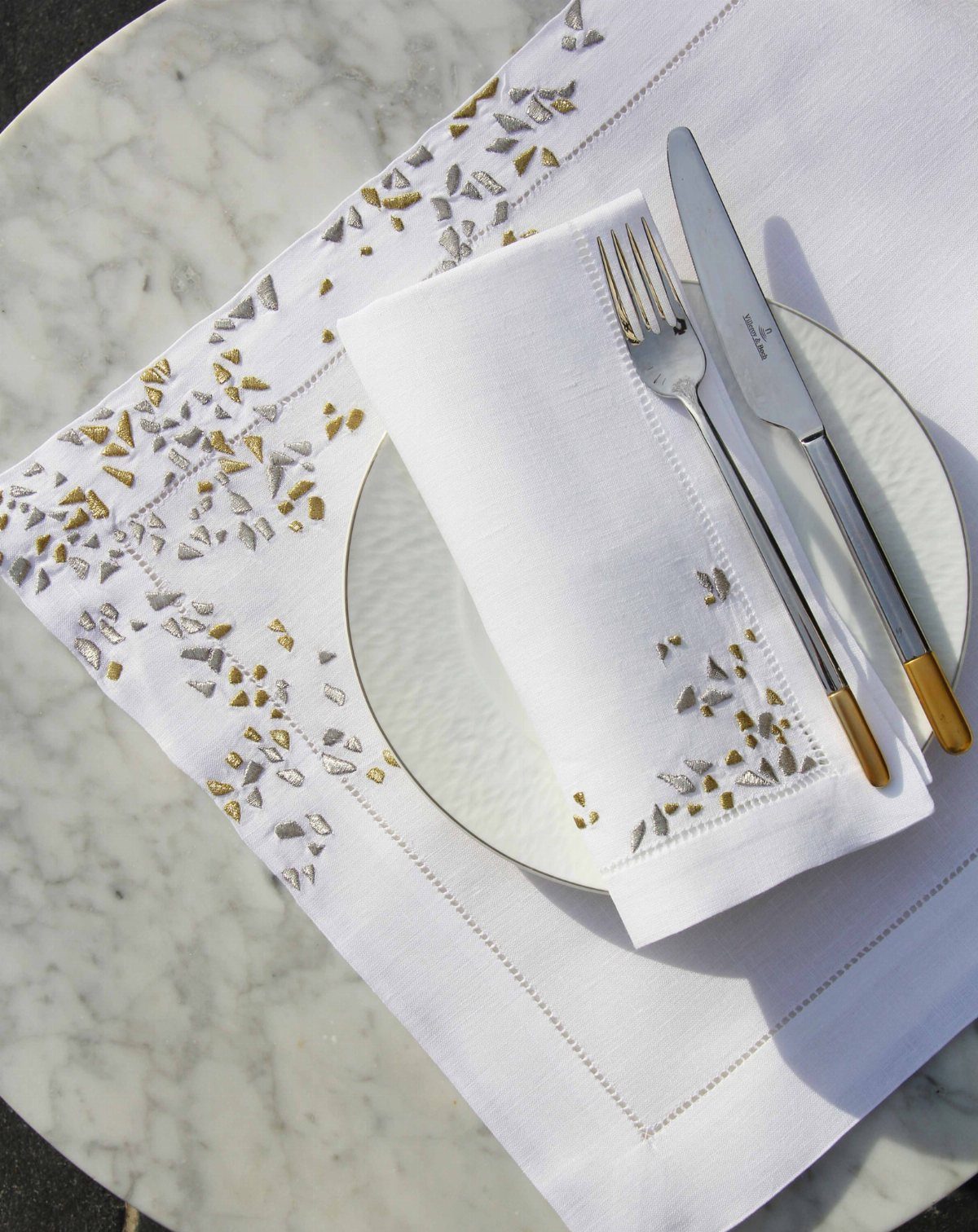 Elegant table setting with embroidered white place mat, plate, and gold-handled cutlery.
