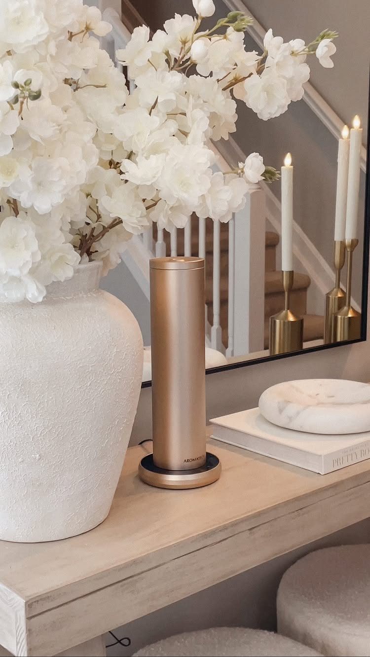 Gold cylindrical essential oil diffuser on a wooden table next to white flowers