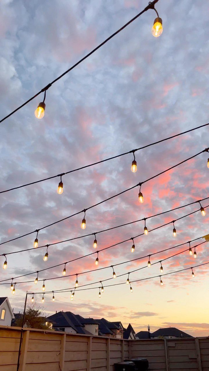 Outdoor string lights glowing against a pink and blue sunset sky over a backyard.