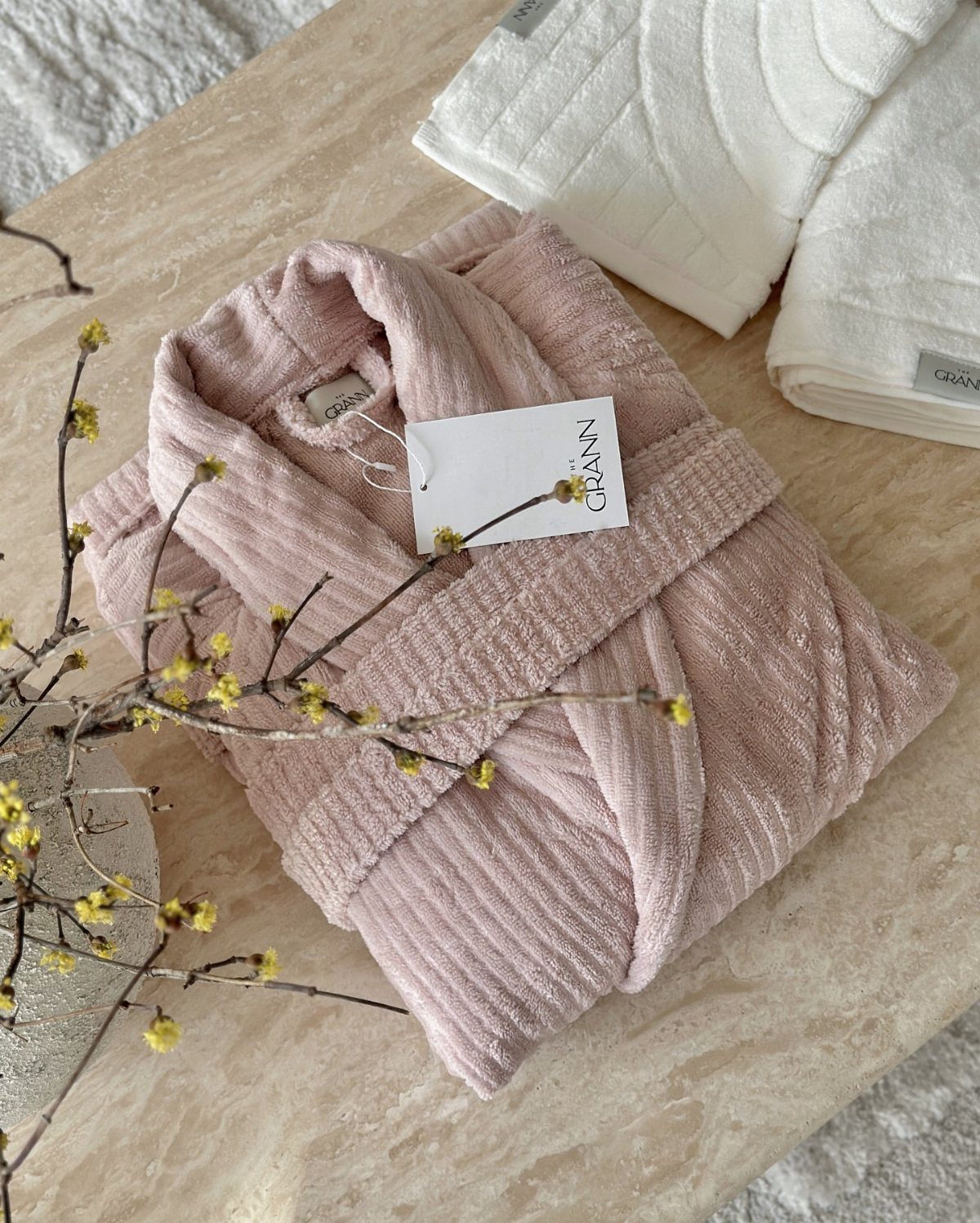 Pink ribbed bathrobe and white towels on a marble surface with yellow flowers.
