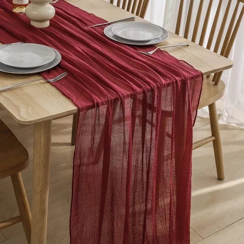 Burgundy sheer table runner on a light wooden dining table with white plates.