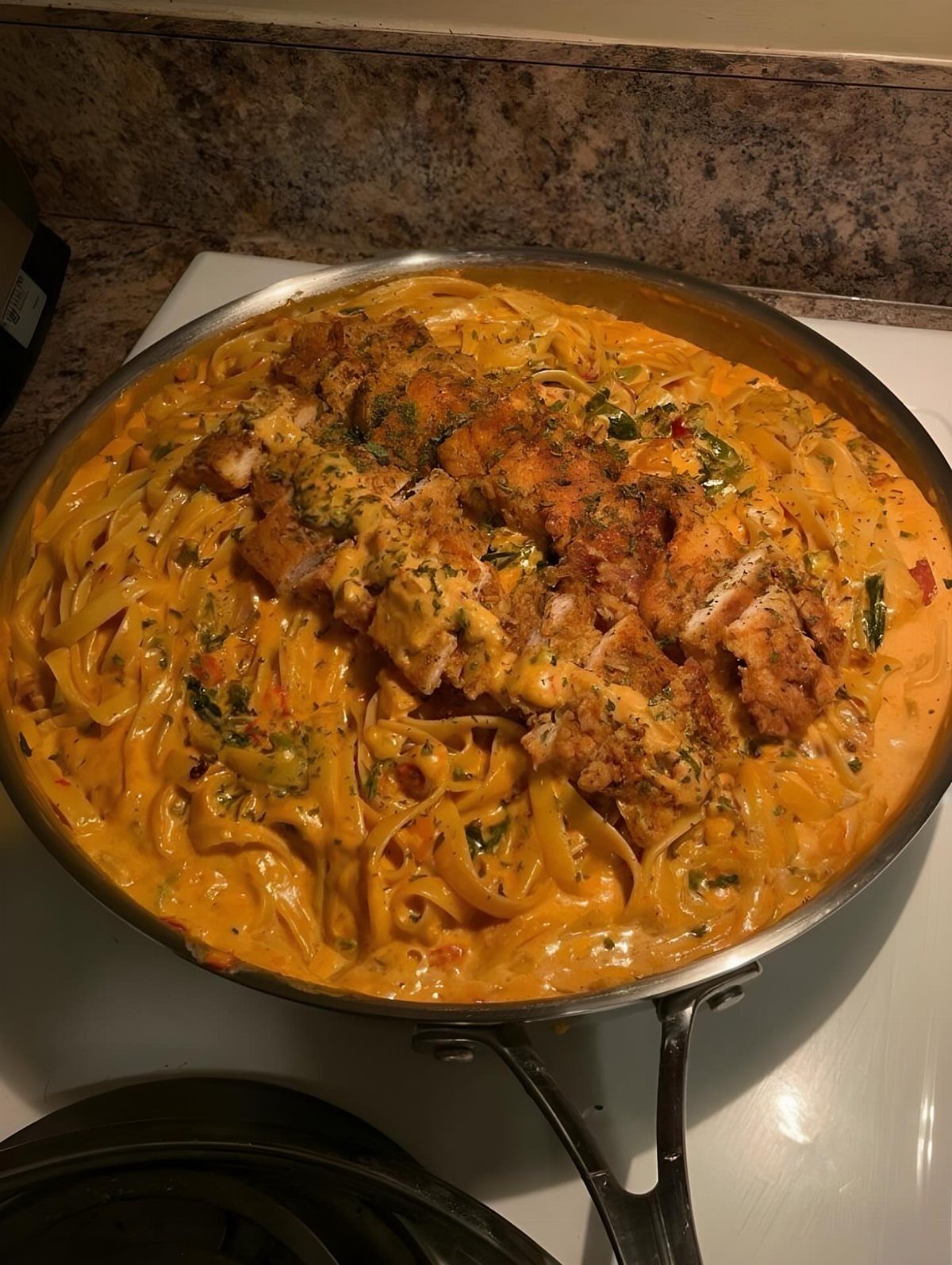 Breaded chicken breasts over creamy pasta in a stainless steel skillet