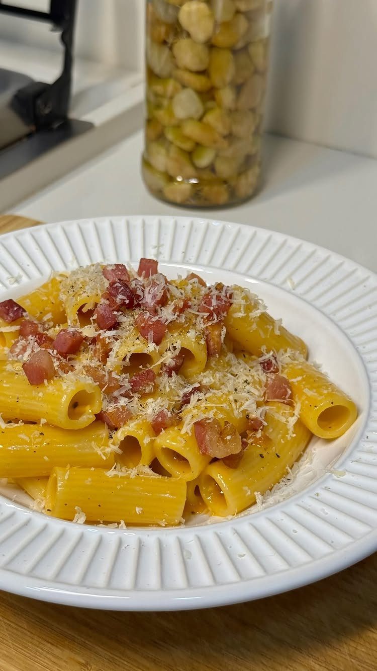 Rigatoni pasta carbonara with pancetta and parmesan cheese on a white fluted plate.