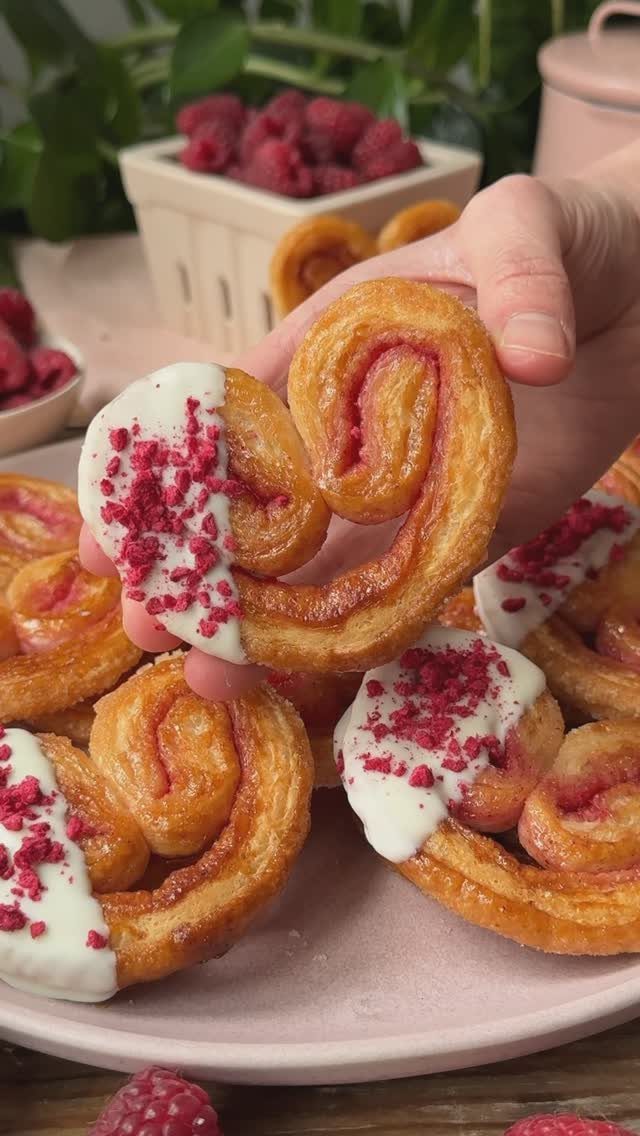 Heart-shaped puff pastry with white icing and raspberry crumbs held over a plate.