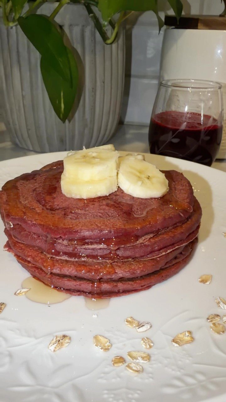Stack of red beet pancakes topped with banana slices and syrup on white plate