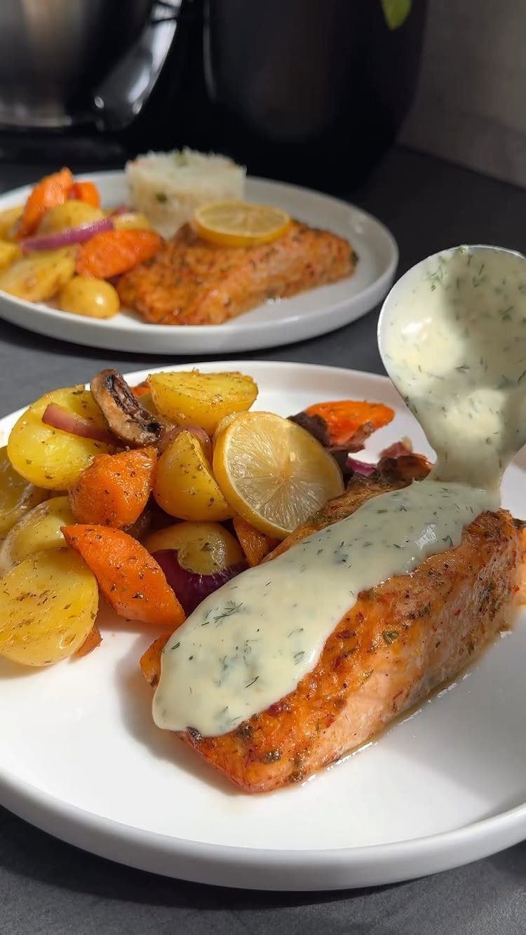 Seared salmon fillets with creamy herb sauce and roasted root vegetables on white plates.