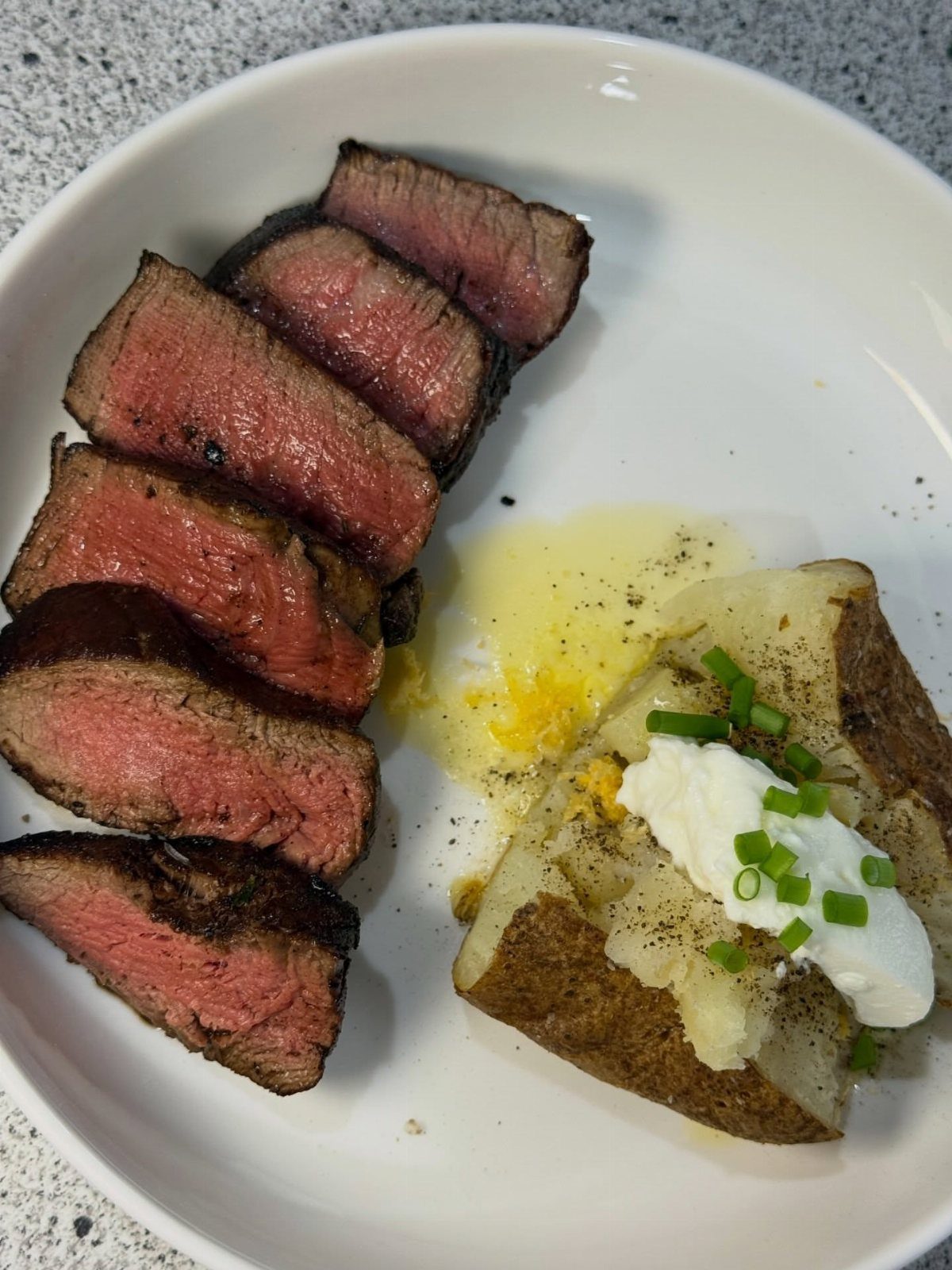 Slices of medium-rare steak and a loaded baked potato on a white plate.