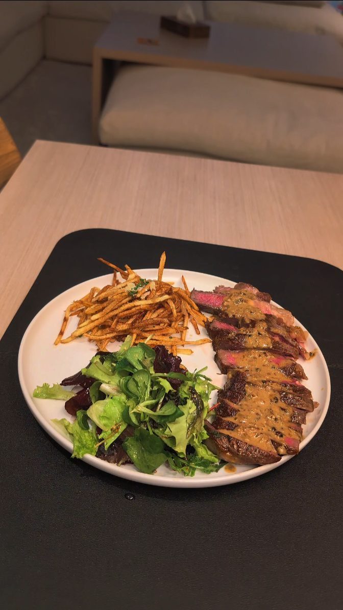 Sliced seared steak with sauce, thin crispy fries, and a fresh green salad.
