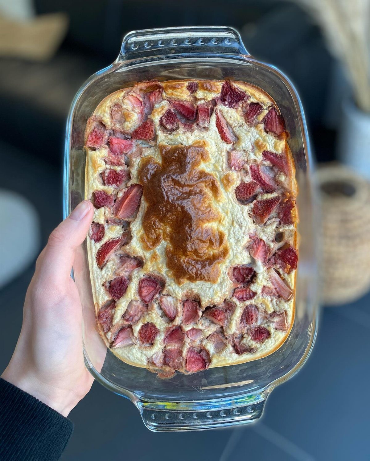 Baked oatmeal with sliced strawberries in a clear glass baking dish held by hand.