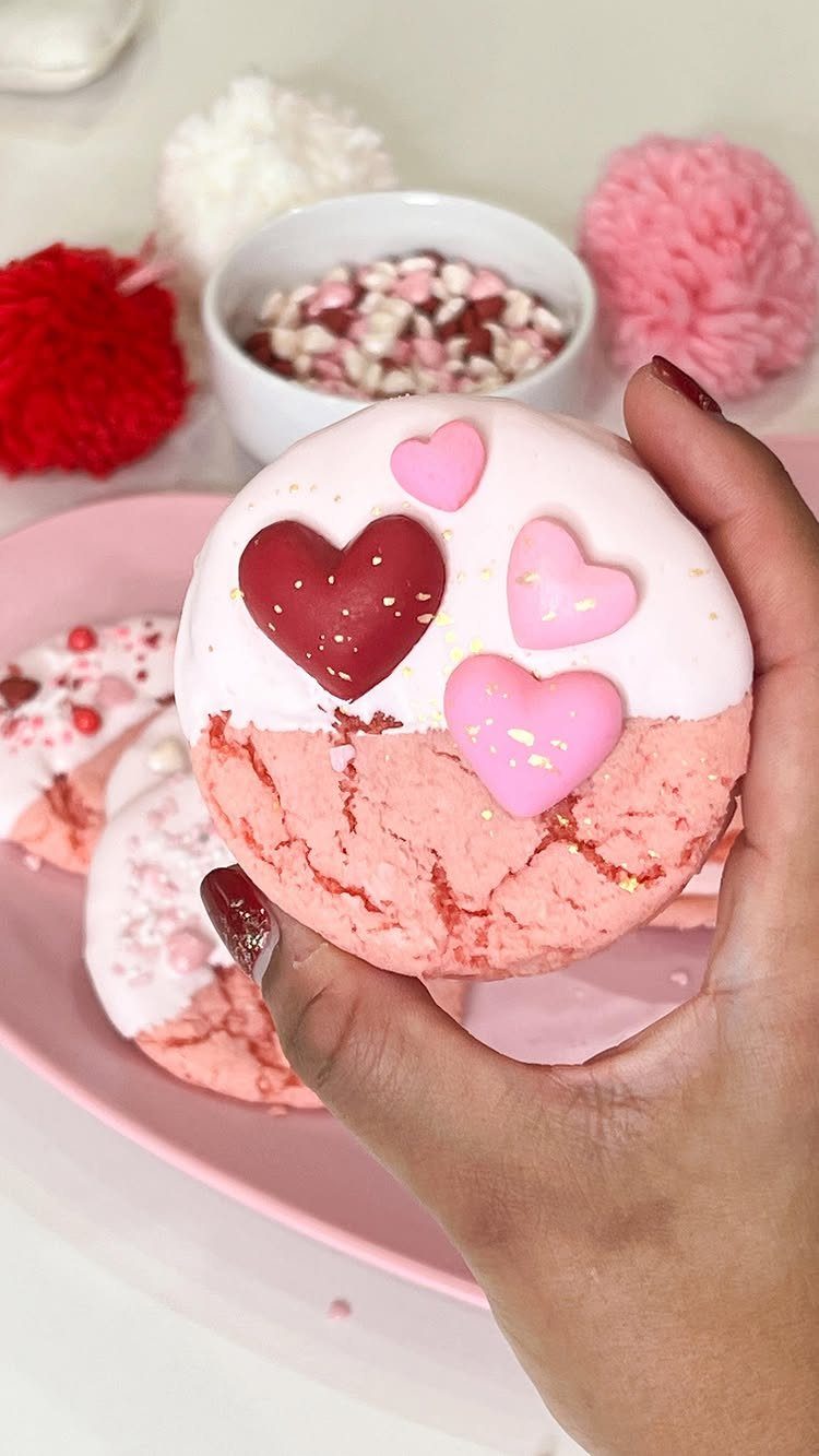 Pink heart-decorated cookies held by a hand over a pink plate.