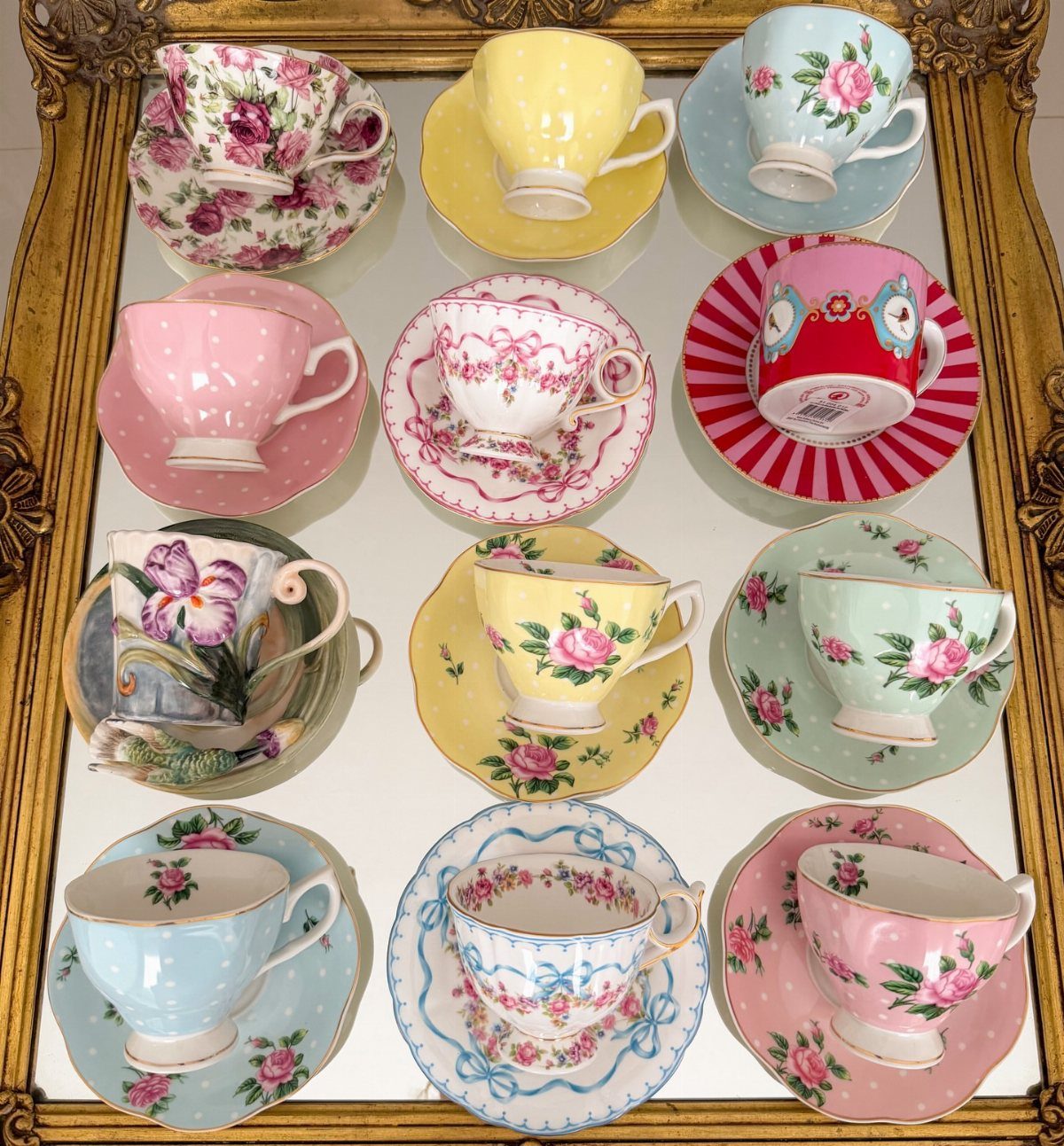 Mismatched vintage floral teacups and saucers arranged on a mirrored gold tray.