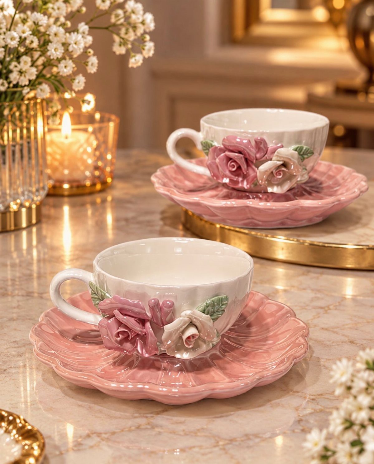 White teacups with sculpted pink roses on pink scalloped saucers on marble surface