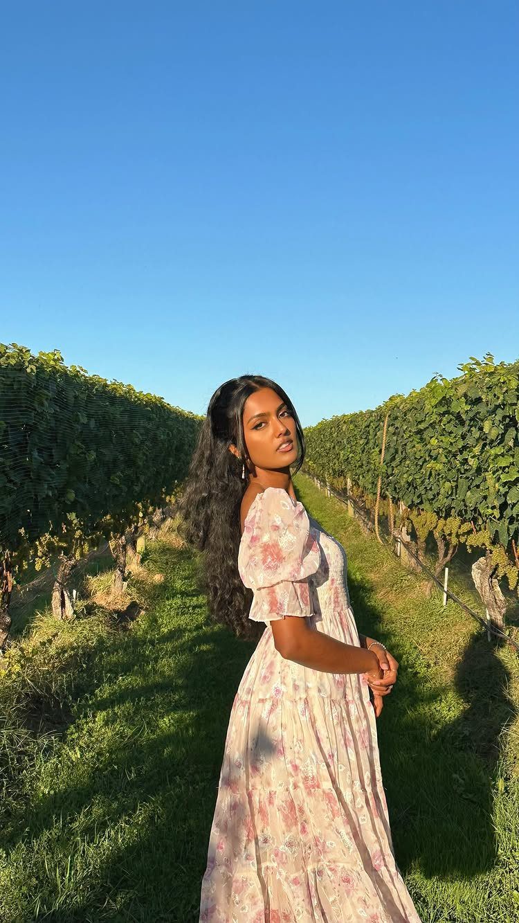 Woman in a floral puff-sleeve dress posing in a sunny green vineyard.