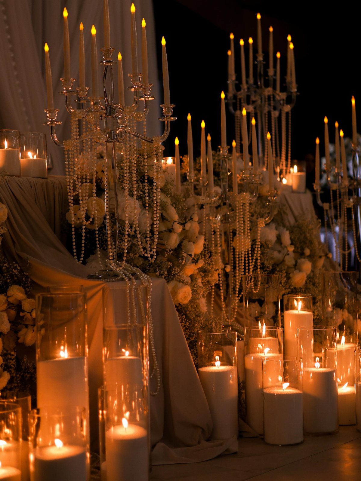 Ornate silver candelabras with lit taper candles and crystals among white pillar candles.