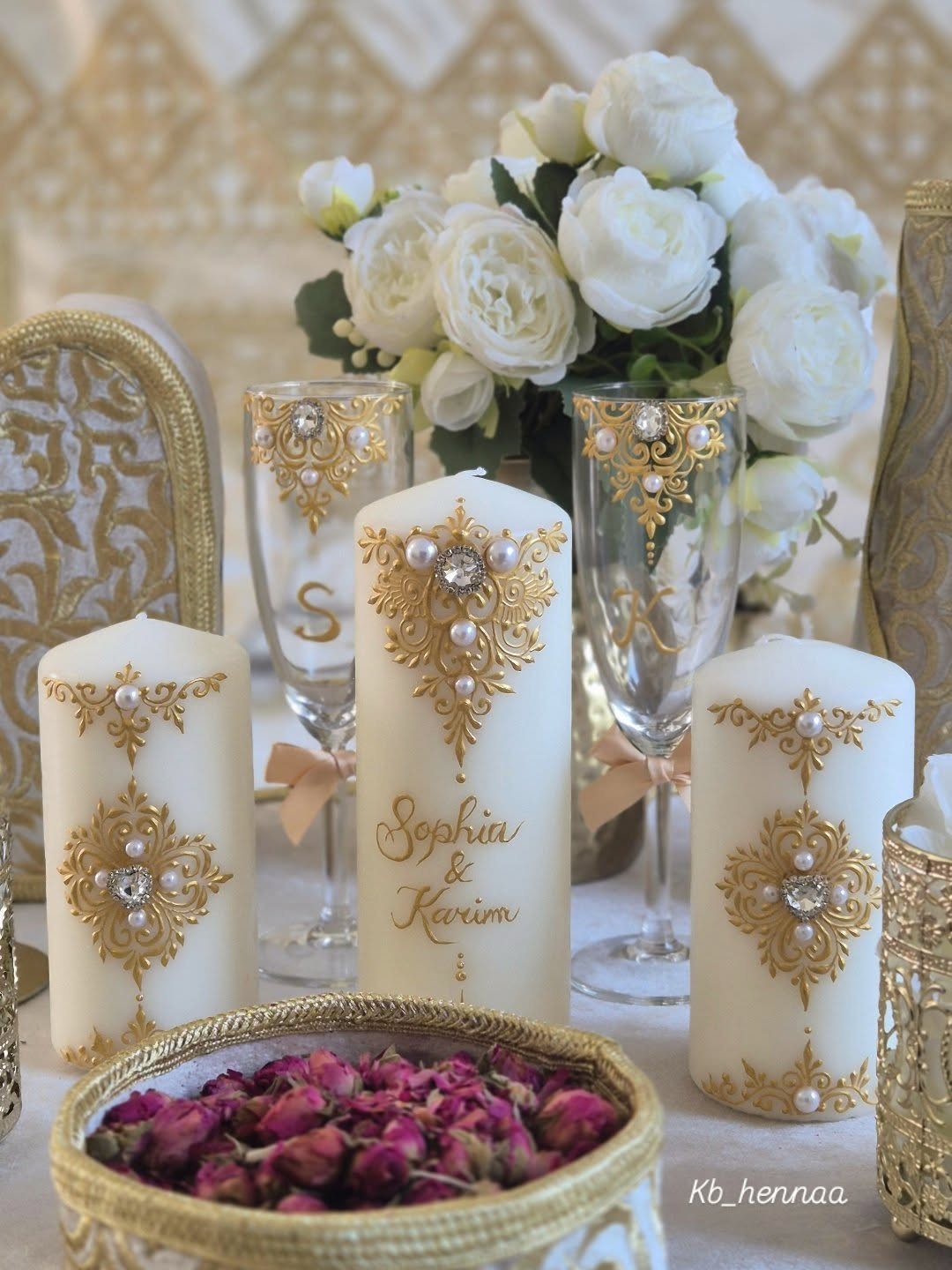 Three white pillar candles with gold decorations arranged on a wedding table.