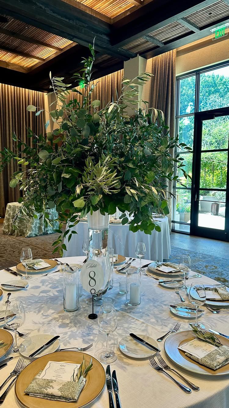 Wedding table centerpiece with lush green foliage and small cylindrical glass candles.