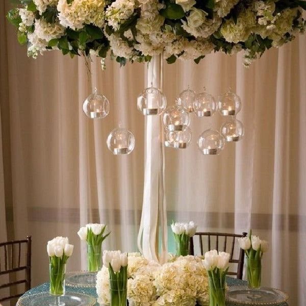 Tall white floral centerpiece with hanging glass candle globes on a wedding table