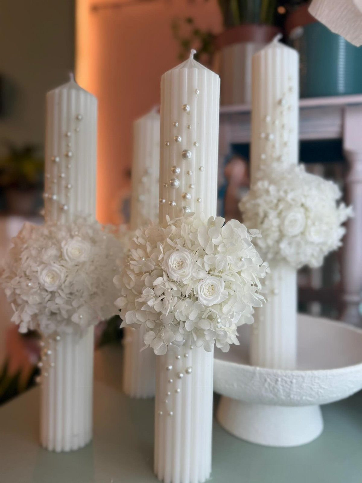 White ribbed pillar candles decorated with pearls and white floral arrangements.