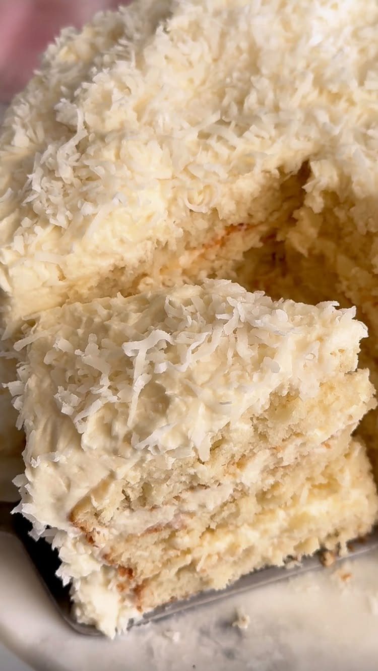White layered cake covered in shredded coconut with one slice being served.