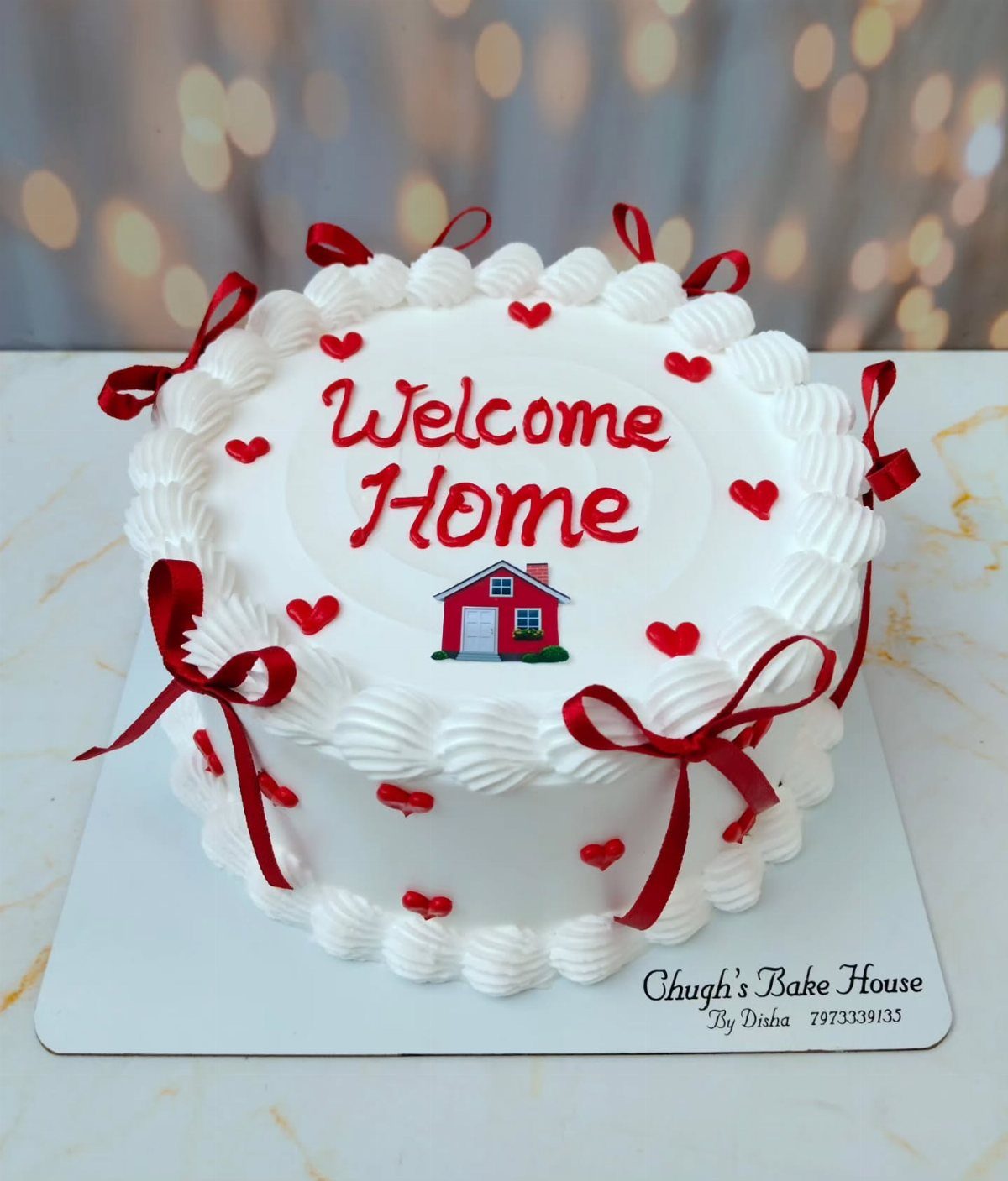 White welcome home cake with red hearts, ribbons, and a small red house.