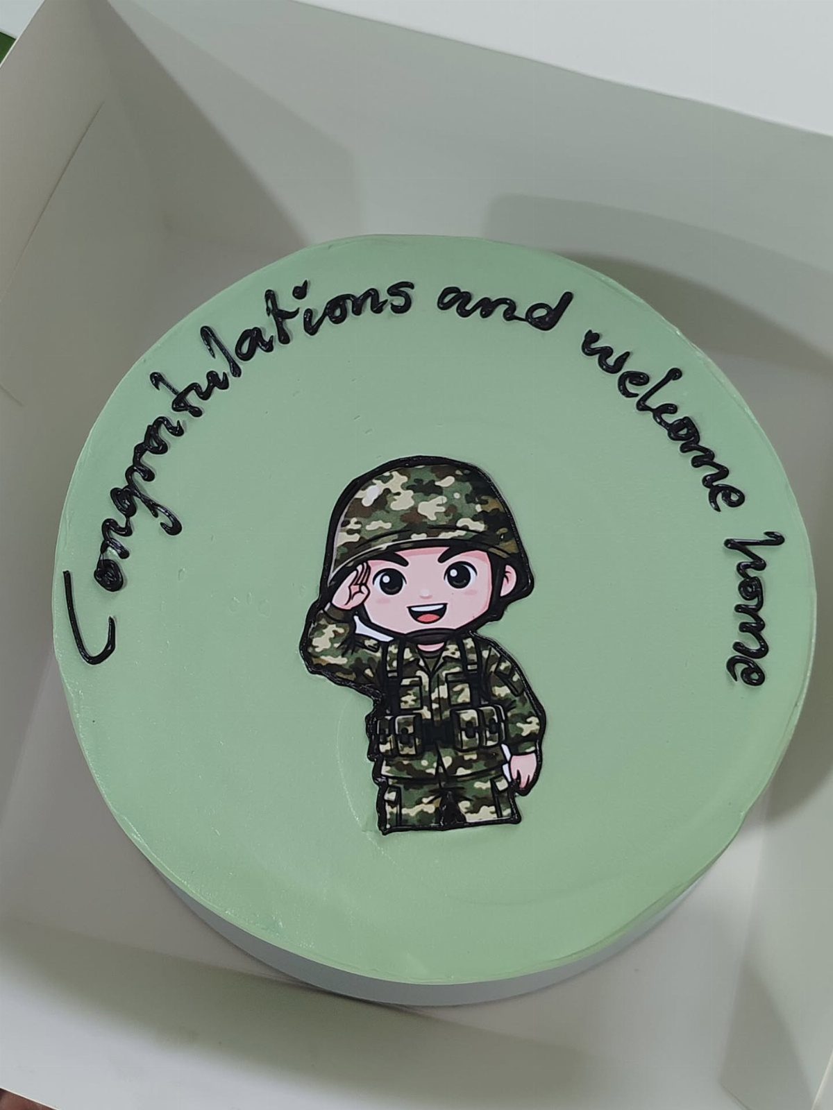 Light green cake with a saluting soldier illustration and welcome home icing text.