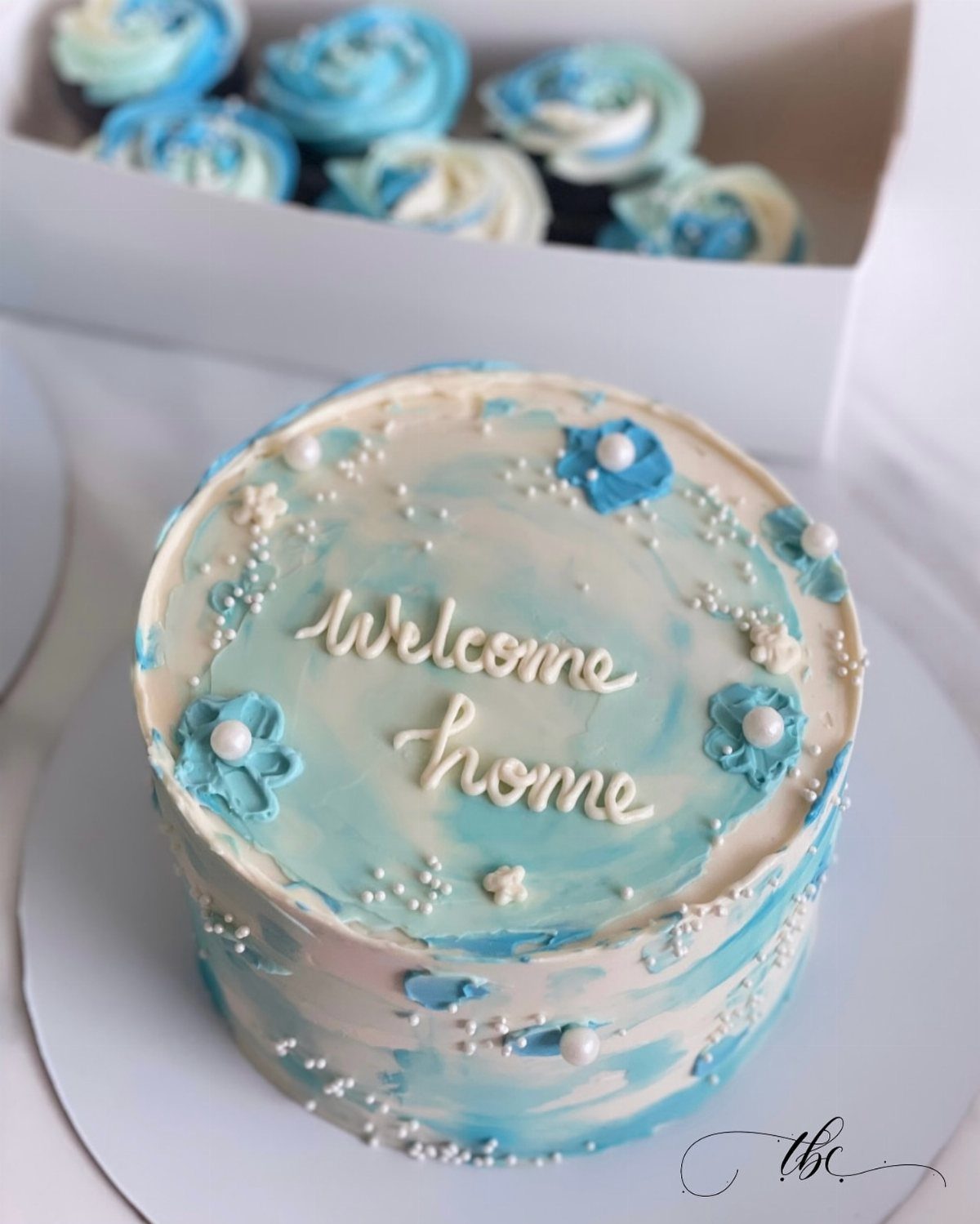 Blue and white swirled cake with Welcome home icing and blue frosting flowers.