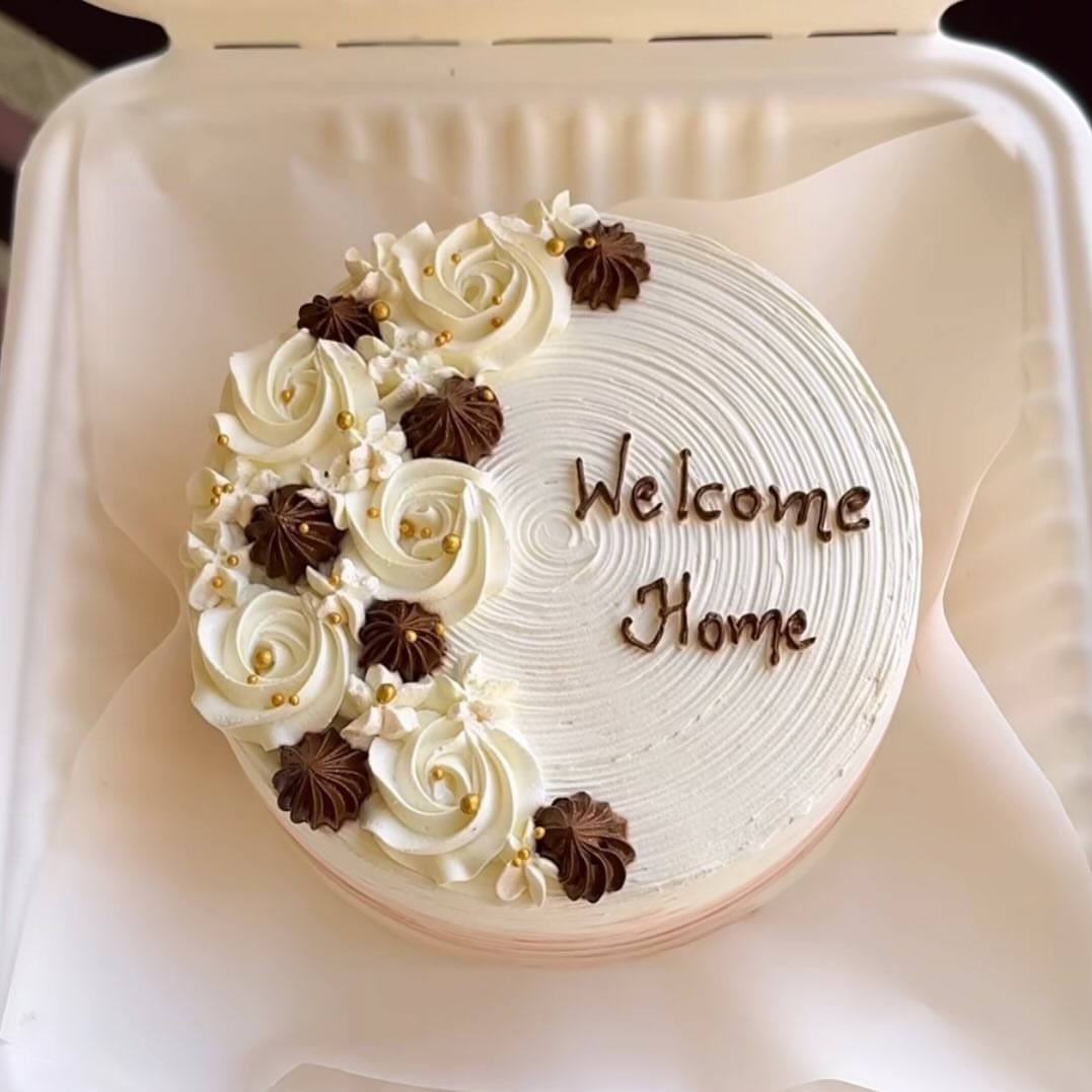White welcome home cake with chocolate and white frosting rosettes and gold pearls.
